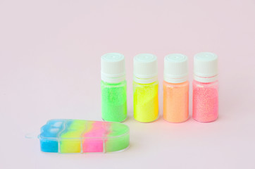 Colorful glitters lies on pastel pink background. Many round jars with multi-colored bright sparkles for nail polish. Sparkling sequins