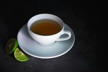 cup of tea on a rough black texture and crescent lime, dark background