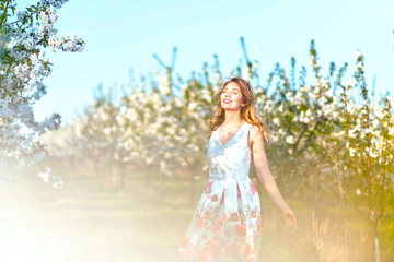 Happy Woman in an orchard at springtime. Enjoying sunny warm day. Retro style dress. Blooming blossom cherry trees. Colorful spring moods