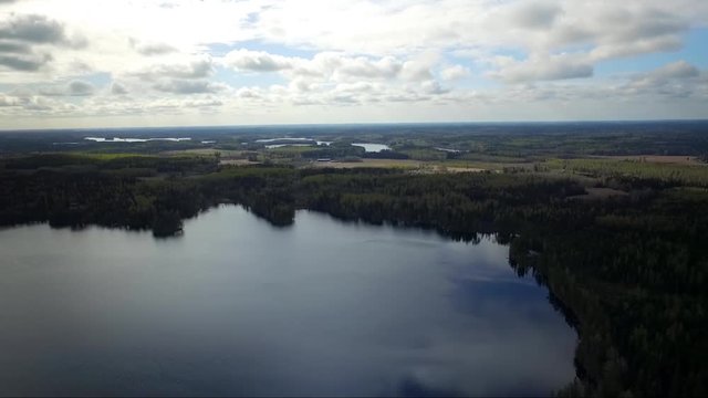 Aerial drone shot of lakes, forest and fields. Flying over Finland landscape. Reflection. Mirror surface lake water.