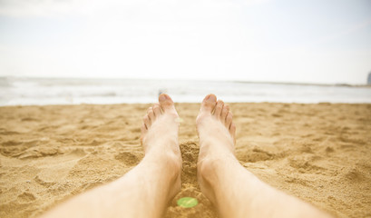 Man is relaxing barefoot at the beach. Guy's legs on the sand. Waves at the ocean side. Coastline...