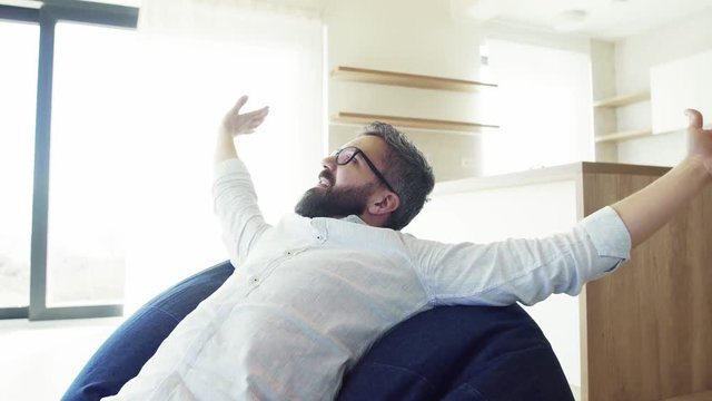 Cheerful Mature Man Sitting On Bean Bag In Unfurnished House.