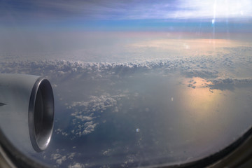 Airplane window overlooking the beautiful clouds and the earth. Sunset in flight on vacation. Tourist theme. Stock photo