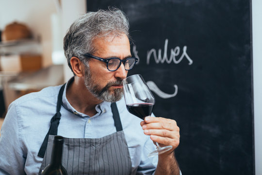 gray haired middle aged man tasting red wine while cooking in his home kitchen