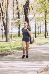 Obraz premium pretty young woman holding smartphone and listening music in earphones while running in park