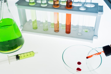 Erlenmeyer flask, Petri dish, Test tubes and a syringe with drops of blood inside is placed on...