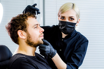 A professional beautician in a black uniform performs the procedure of rejuvenation of the skin of a middle-aged man in a cosmetology clinic