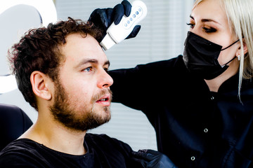 A man sitting in the office of a beautician, the doctor makes the patient hardware facial cleansing