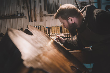 Young luthier working in his workshop, building a double bass
