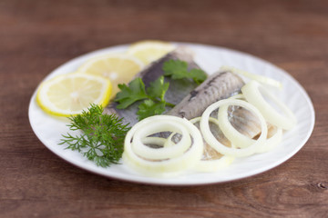 delicious tender herring fillet with lemon,herbs and onion on white plate on wooden background