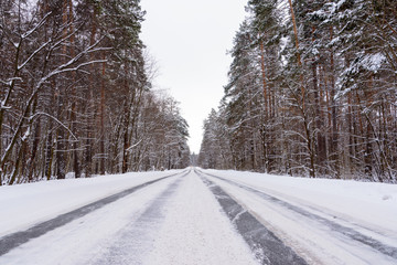 Patterns on the winter highway in the form of four straight lines. Snowy road on the background of forest. Winter landscape.
