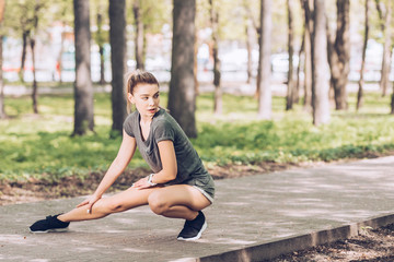 attractive young woman in sportswear looking away while exercising in sunny park