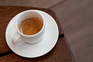 Italian espresso in a white ceramic cup with saucer on a brown wood table. Brurred background.