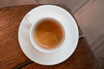 Italian espresso in a white ceramic cup with saucer on a brown wood table from above. Brurred background.