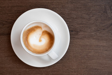 Espresso macchiato in white ceramic cup with saucer isolated on brown wood surface from above. Space for text.