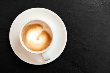 Espresso macchiato in white ceramic cup with saucer isolated on black leather surface from above. Space for text.