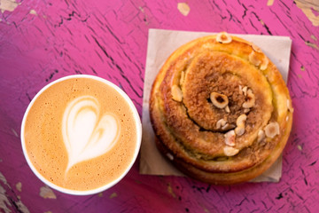 Cappuccino and cinnamon pastry roll isolated on peeling and cracked pink painted wood from above.