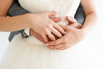 Young married couple holding hands with rings on white background, ceremony wedding day