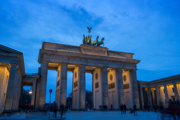Many tourists hanging out at the famous and illuminated neoclassical Brandenburg Gate (Brandenburger Tor) in Berlin, Germany, at dusk.