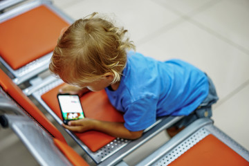 Cute little boy watching cartoons on smartphone in empty waiting room