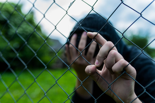 Young unidentifiable teenage boy holding the wired garden at the correctional institute , covering hes face , conceptual image of juvenile delinquency, focus on the boys hand.
