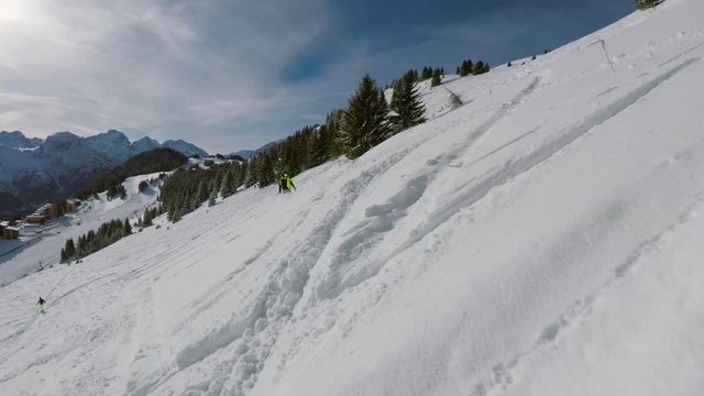 Snowboarder in a bright yellow and black jacket making his way down the side of a slope in deep soft snow. Beautiful scenic view of winter sports paradise of the Alps.