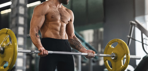 Fototapeta na wymiar Muscular guy lifting heavy barbell at gym
