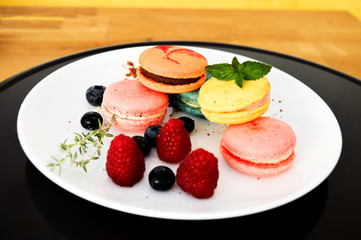 Colorful macaroons on the white plate with raspberries and blueberries