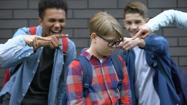 Schoolchildren pointing fingers at junior student, mocking smart boy, bullying