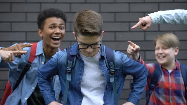 Cruel schoolchildren pointing fingers at student, mocking smart boy, bullying