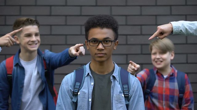 Group of teenagers pointing fingers and laughing at black boy, racial bullying