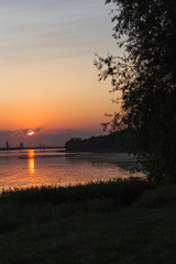 sunset sun in the clouds, river in the evening and summer landscape