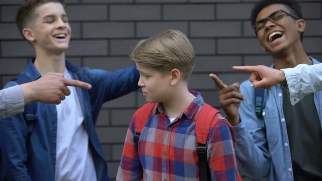 Malicious teenagers pointing fingers at boy crying, depressed victim of bullying