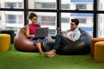 group of creative designers brainstorming together in coworking space . comfortable position . Business man and young African American woman sitting on sofa presenting in  Modern office . drink coffee