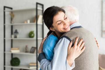 Smiling nurse hugging with grey haired man, standing in room