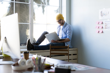Young businessman working on modern loft office. Man sitting by the window, using contemporary notebook.