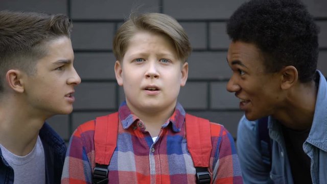 Malicious students teasing boy face-to-face, telling insults, emotional bullying
