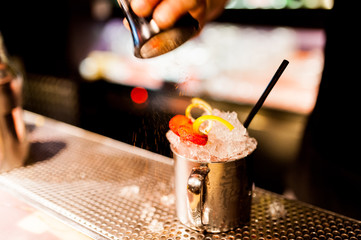 close up of barman hand pouring choco powder on cocktail tin filled with ice and strawberry inside a bar at night