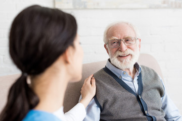 Selective focus of smiling grey haired man looking at nurse - Powered by Adobe