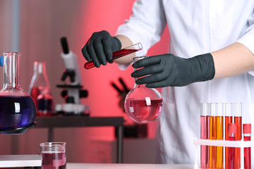 Scientist pouring reagent into flask at table in chemistry laboratory