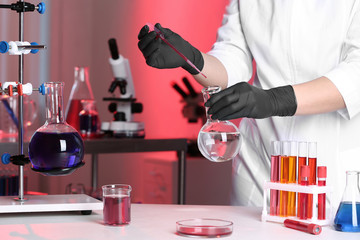 Scientist pouring reagent into flask at table in chemistry laboratory