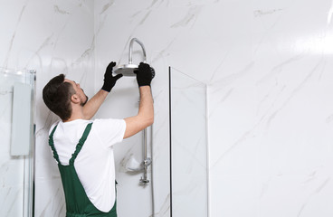 Professional handyman working in shower booth indoors, space for text