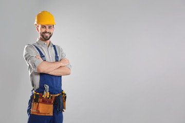 Portrait of professional construction worker with tool belt on grey background, space for text - obrazy, fototapety, plakaty