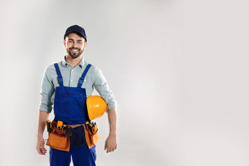 Portrait of construction worker with hard hat and tool belt on light background, space for text