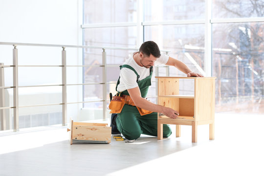 Handyman in uniform assembling furniture indoors. Professional construction tools