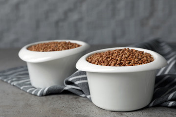 Uncooked buckwheat in bowls on table. Space for text