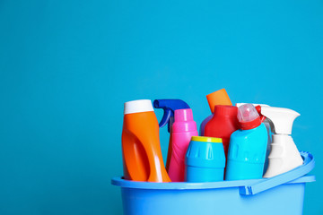 Plastic bucket with different cleaning products against color background. Space for text