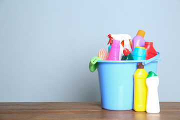 Plastic bucket with different cleaning products on table against color background. Space for text