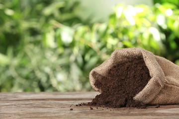 Bag and scattered soil on wooden table against blurred background, space for text. Gardening time