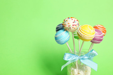 Delicious cake pops in jar full of marshmallows on color background. Space for text